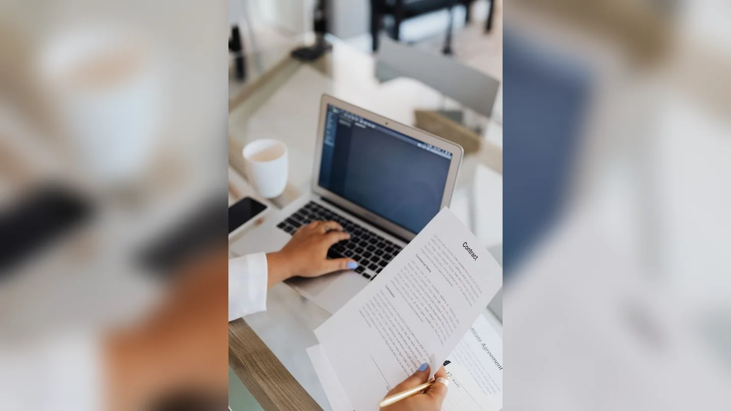 Hands reviewing paperwork beside a laptop