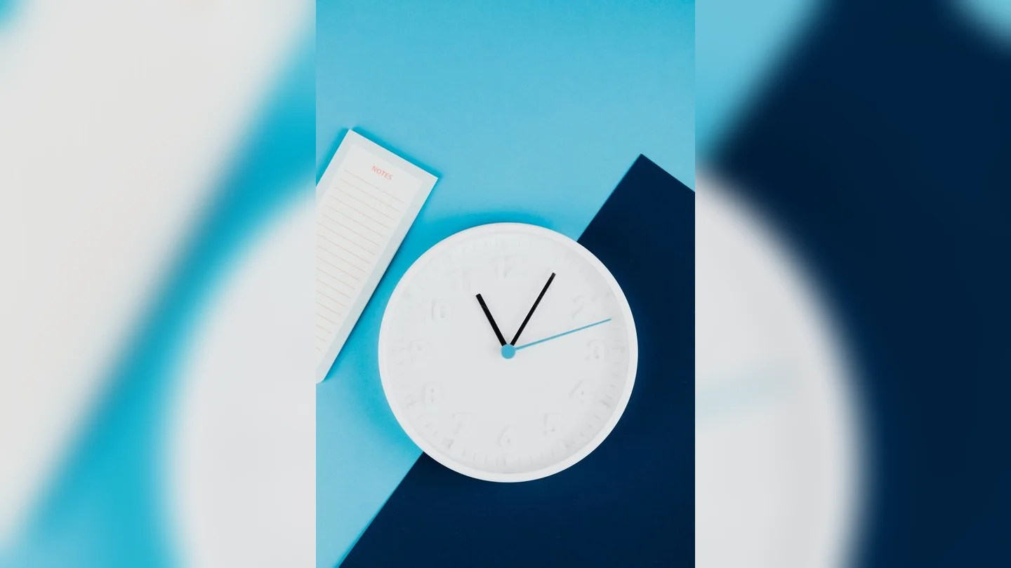 Clock and notebook on a blue desk