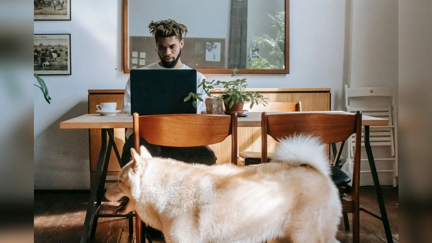 Man using a laptop with his dog beside the table