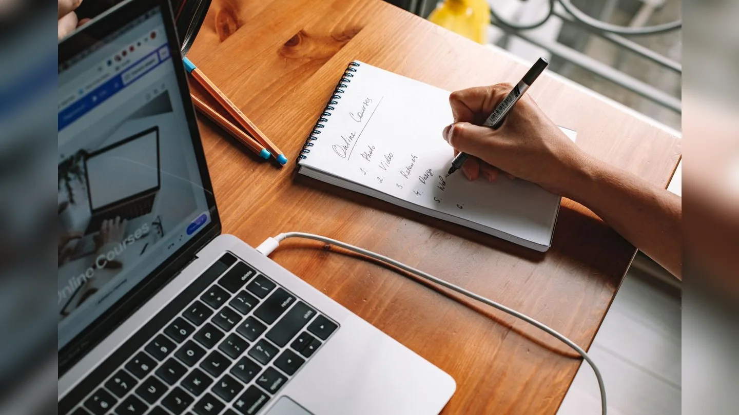 Hands taking notes beside a laptop