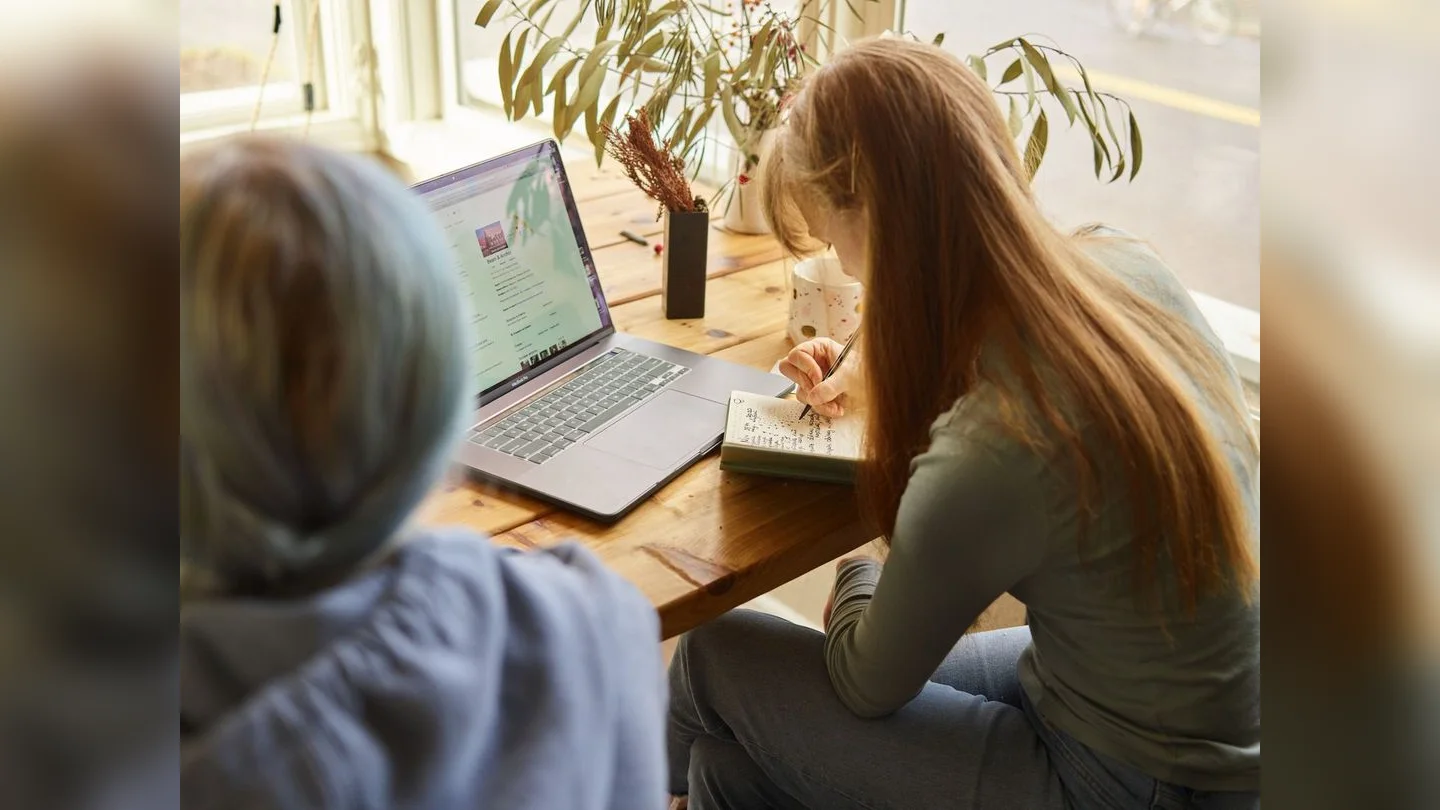 Person taking notes beside a laptop