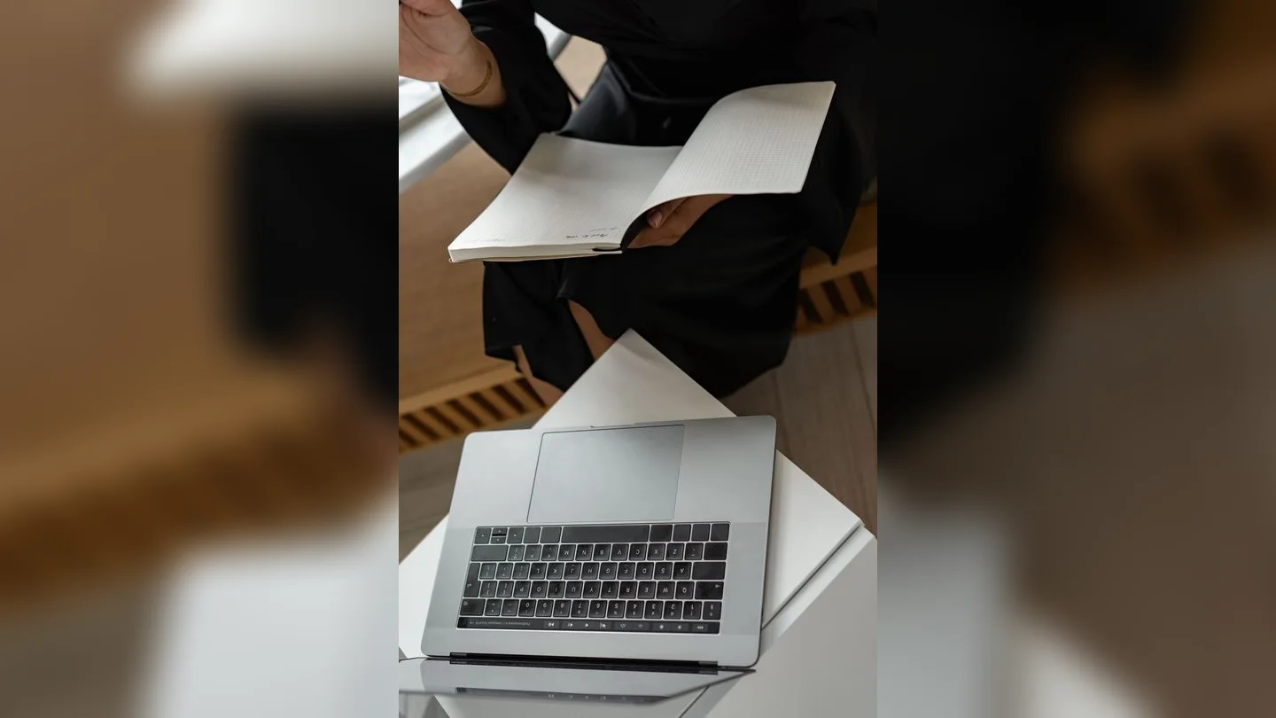 Person reviewing a notebook beside a laptop